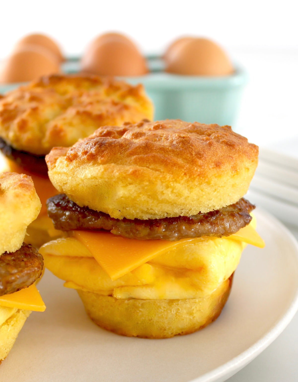 closeup of Keto Sausage Egg and Cheese Biscuits on white plate with eggs in back