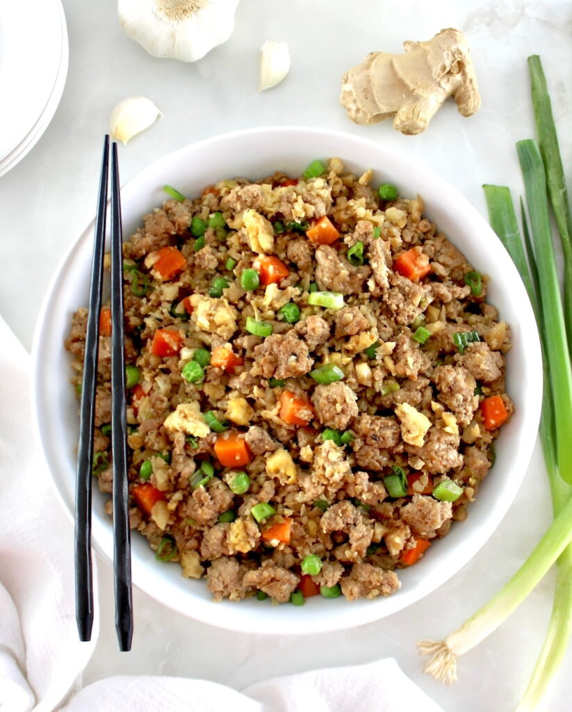 overhead view of Pork Fried Cauliflower Rice in white bowl with black chopsticks on side