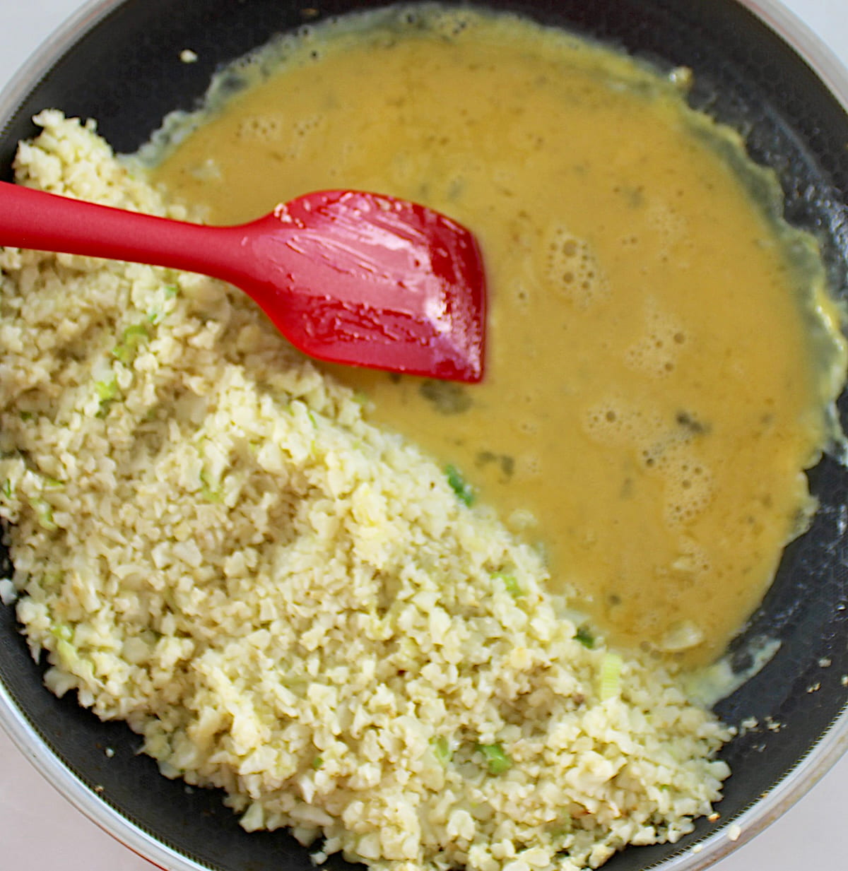 cauliflower rice in skillet with scrambled eggs on side with red spatula