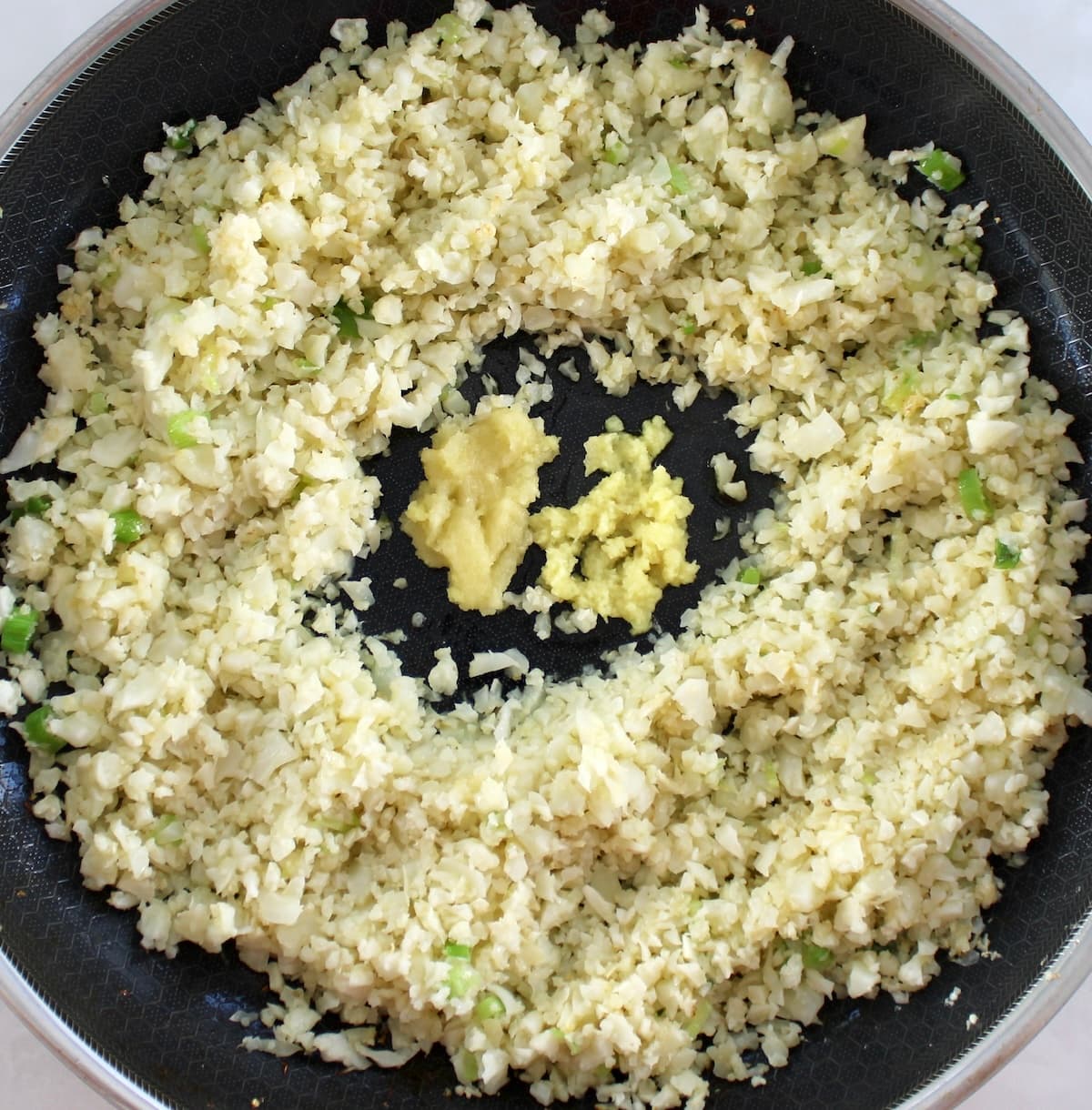 cauliflower rice in skillet with grated garlic and ginger in center