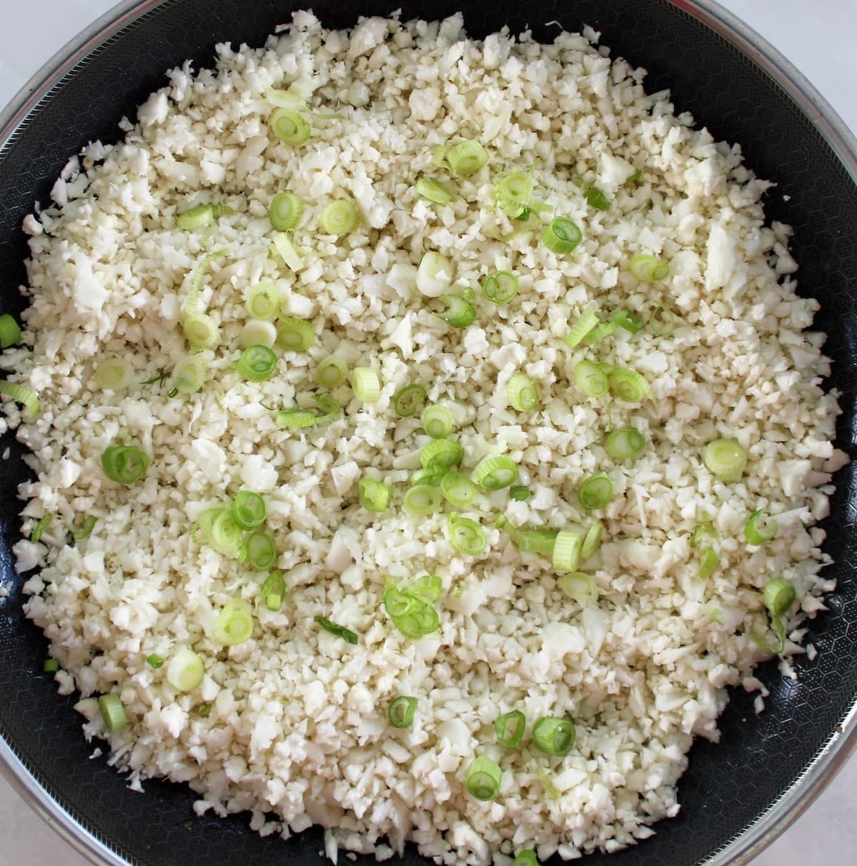 cauliflower rice and scallions cooking in skillet