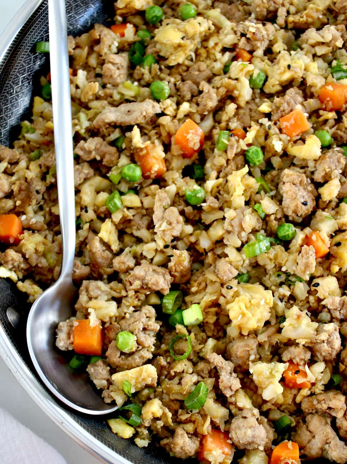 closeup of Pork Fried Cauliflower Rice in skillet with silver serving spoon on side