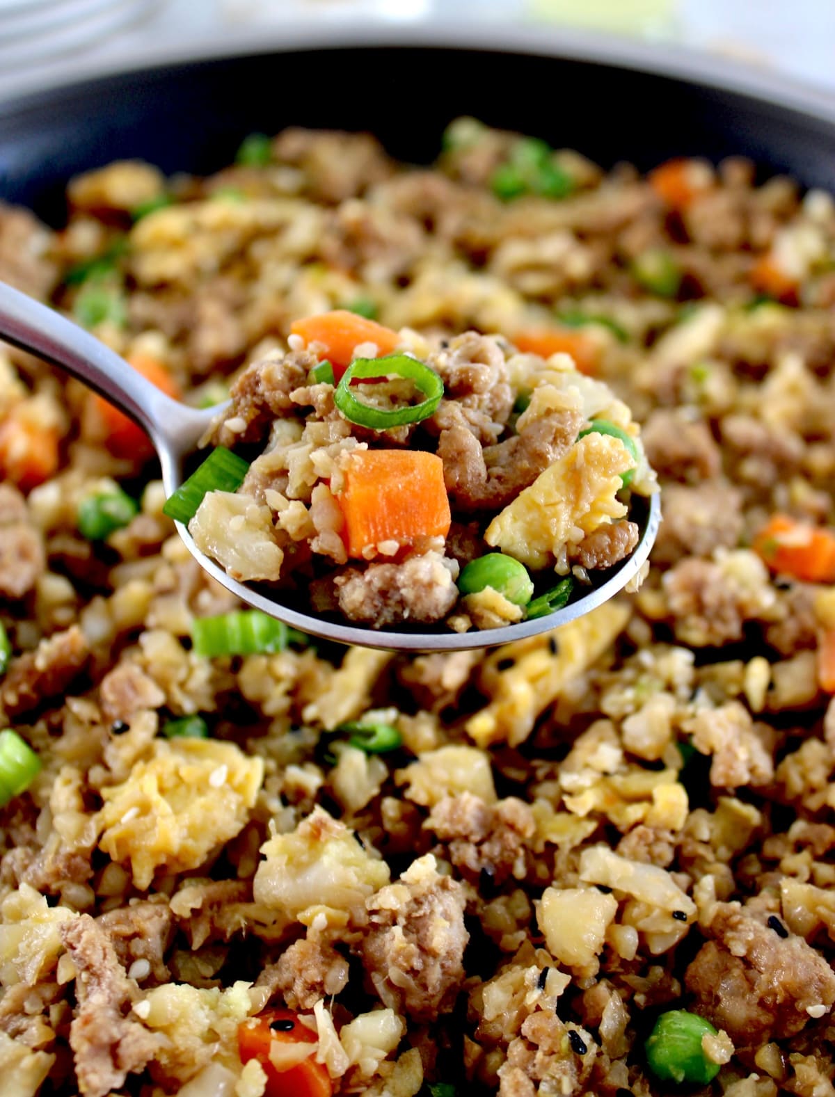 closeup of Pork Fried Cauliflower Rice in spoon held up over skillet