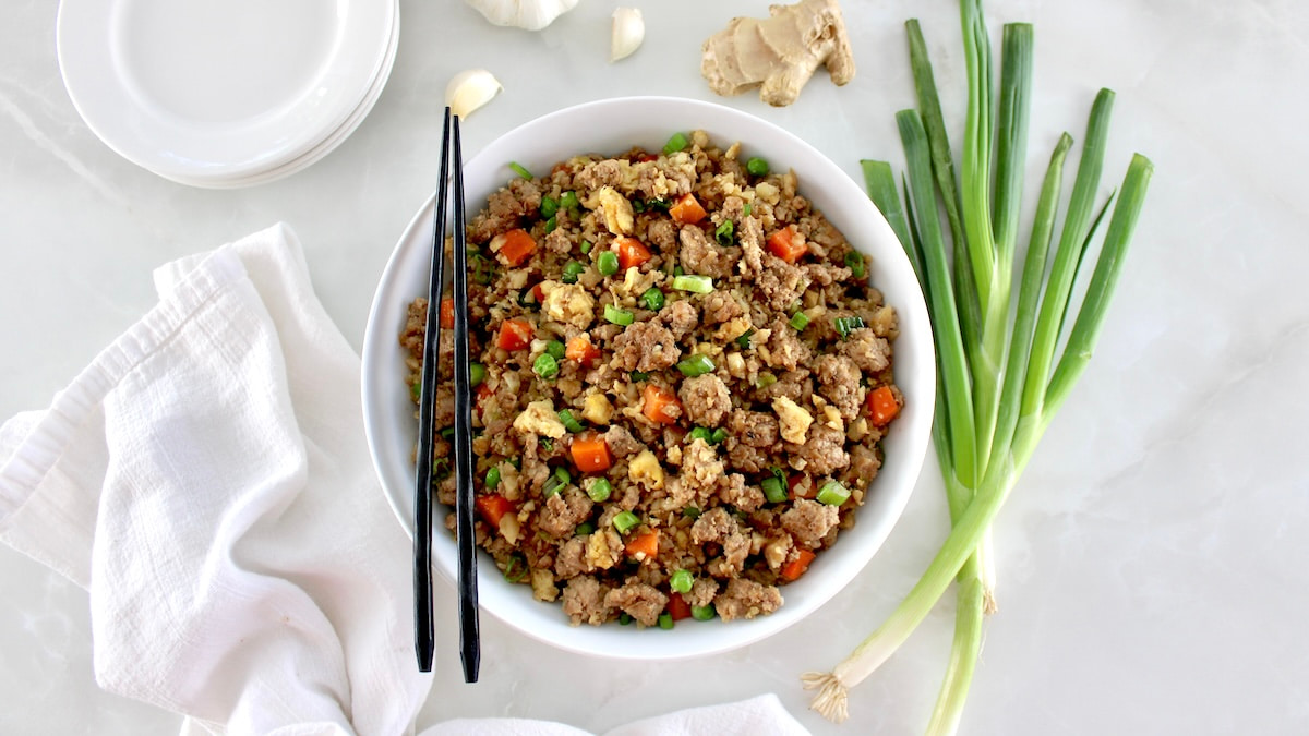 overhead view of Pork Fried Cauliflower Rice in white bowl with black chopsticks on side