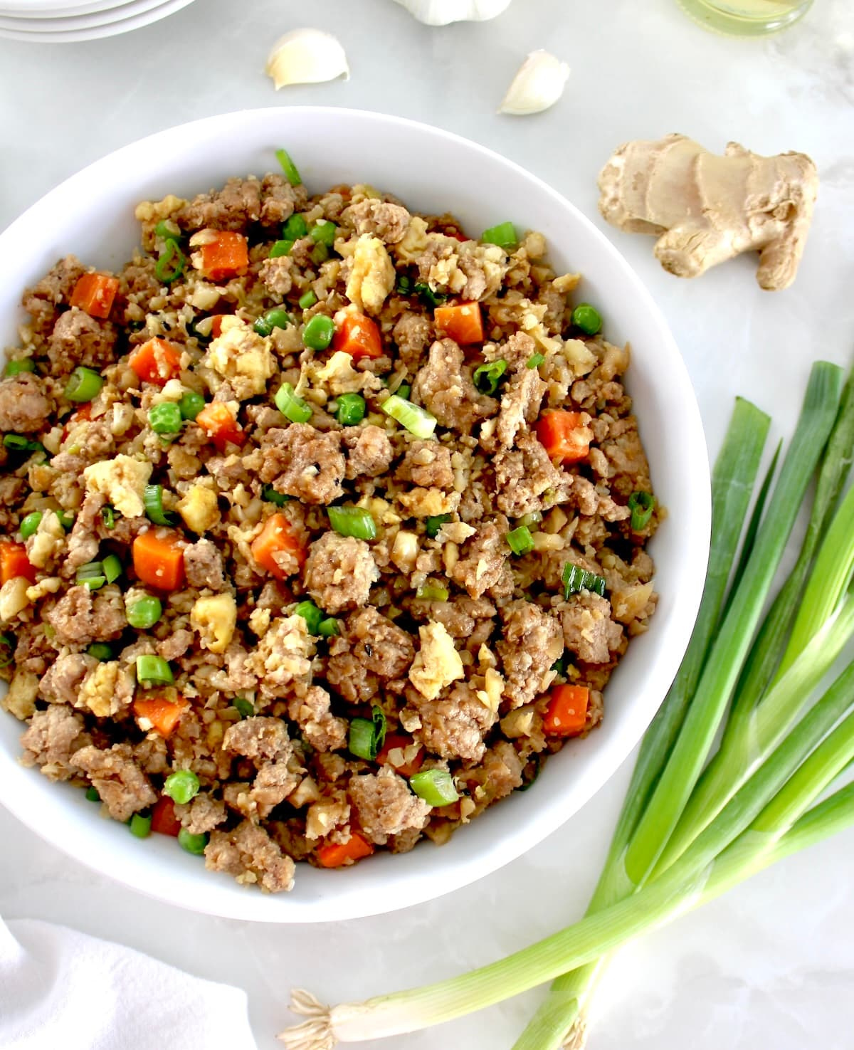 overhead view of Pork Fried Cauliflower Rice in white bowl with scallions on side