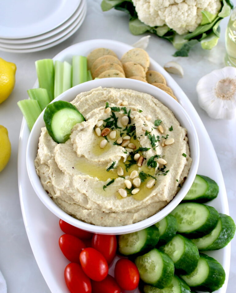 Roasted Garlic Cauliflower Hummus in white bowl with fresh veggies around