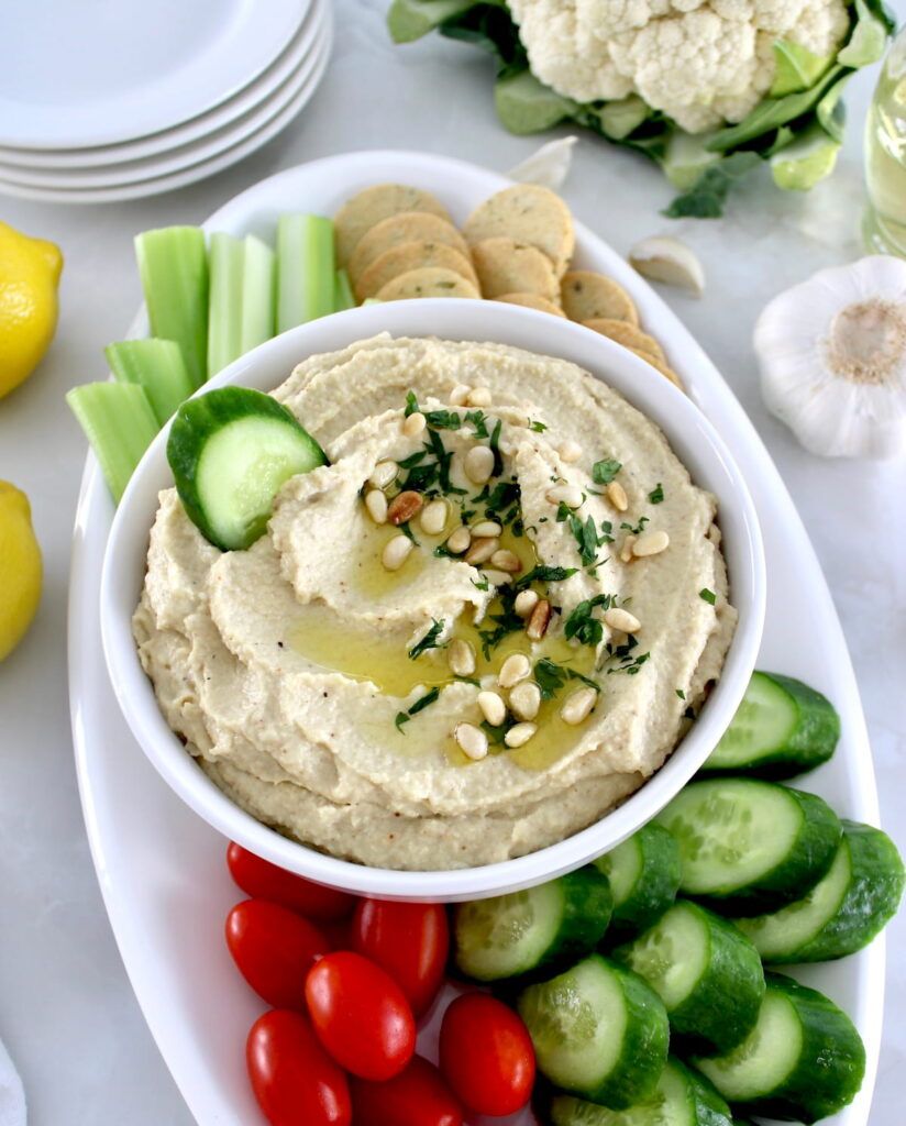 Roasted Garlic Cauliflower Hummus in white bowl with fresh veggies around