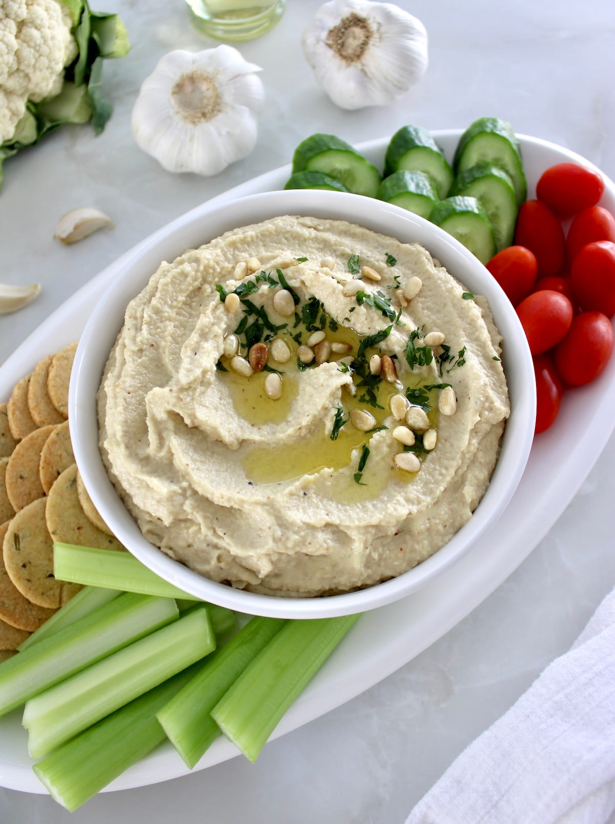 overhead view of Roasted Garlic Cauliflower Hummus on white platter with fresh veggies and crackers around
