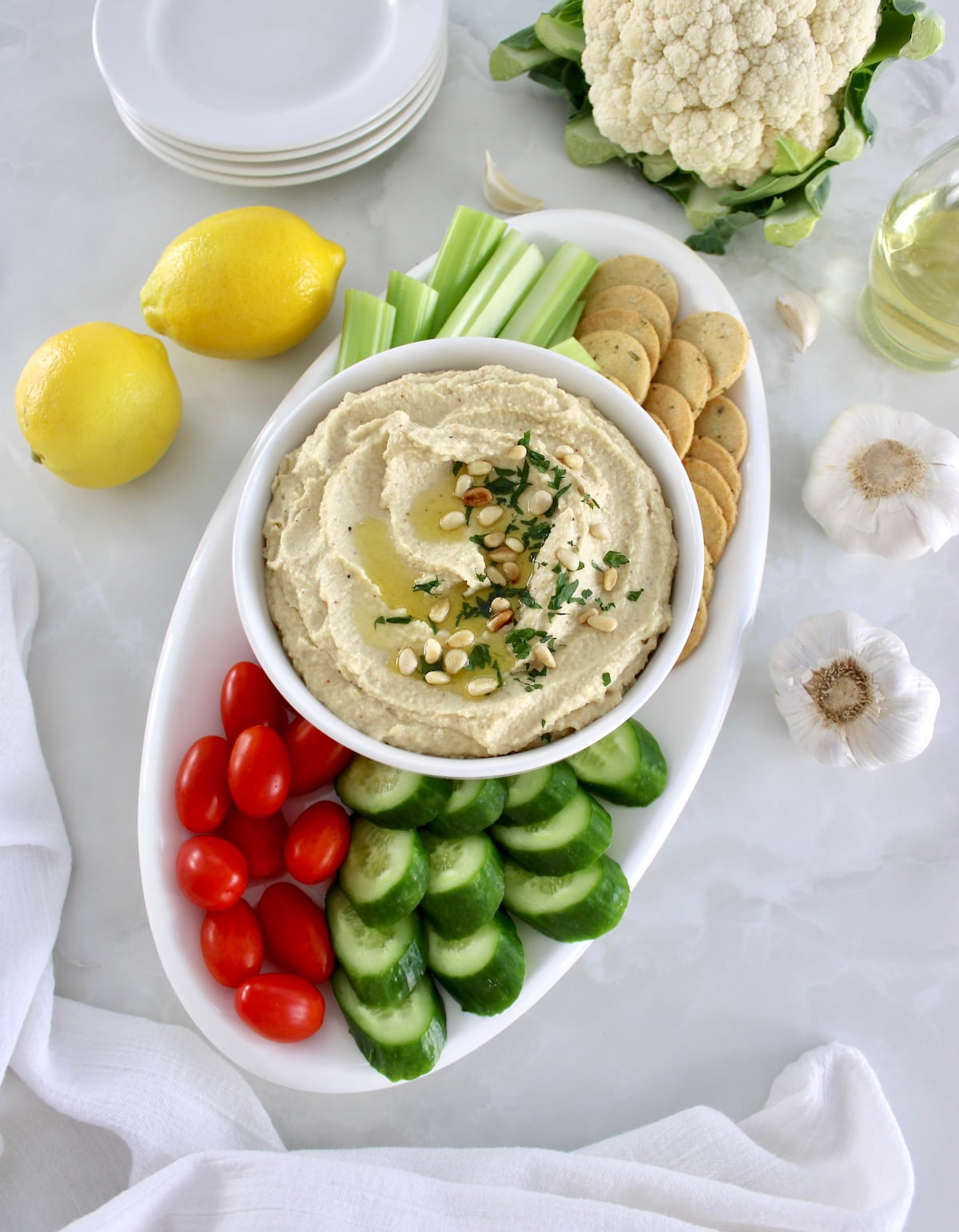 overhead view of Roasted Garlic Cauliflower Hummus on white oval platter with fresh veggies and crackers around