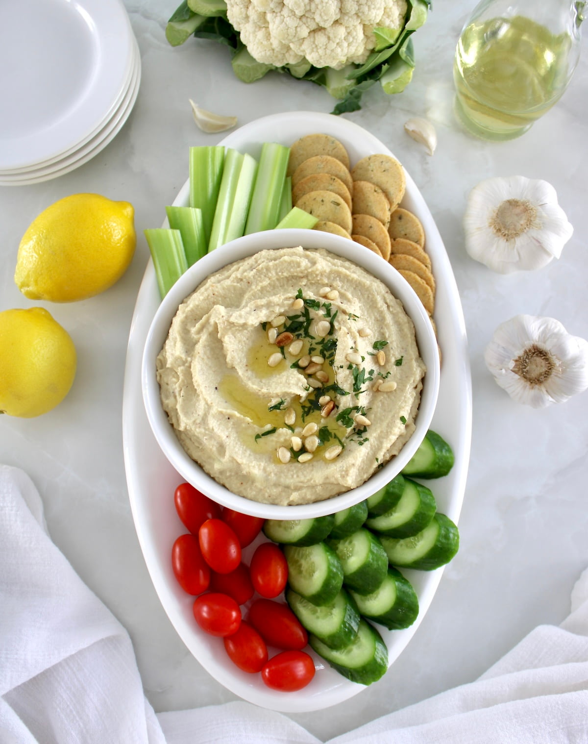 overhead view of Roasted Garlic Cauliflower Hummus on white oval platter with fresh veggies and crackers around