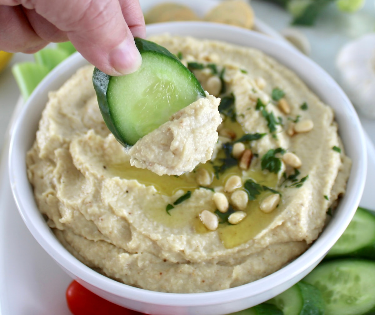 holding up cucumber dipped in Roasted Garlic Cauliflower Hummus