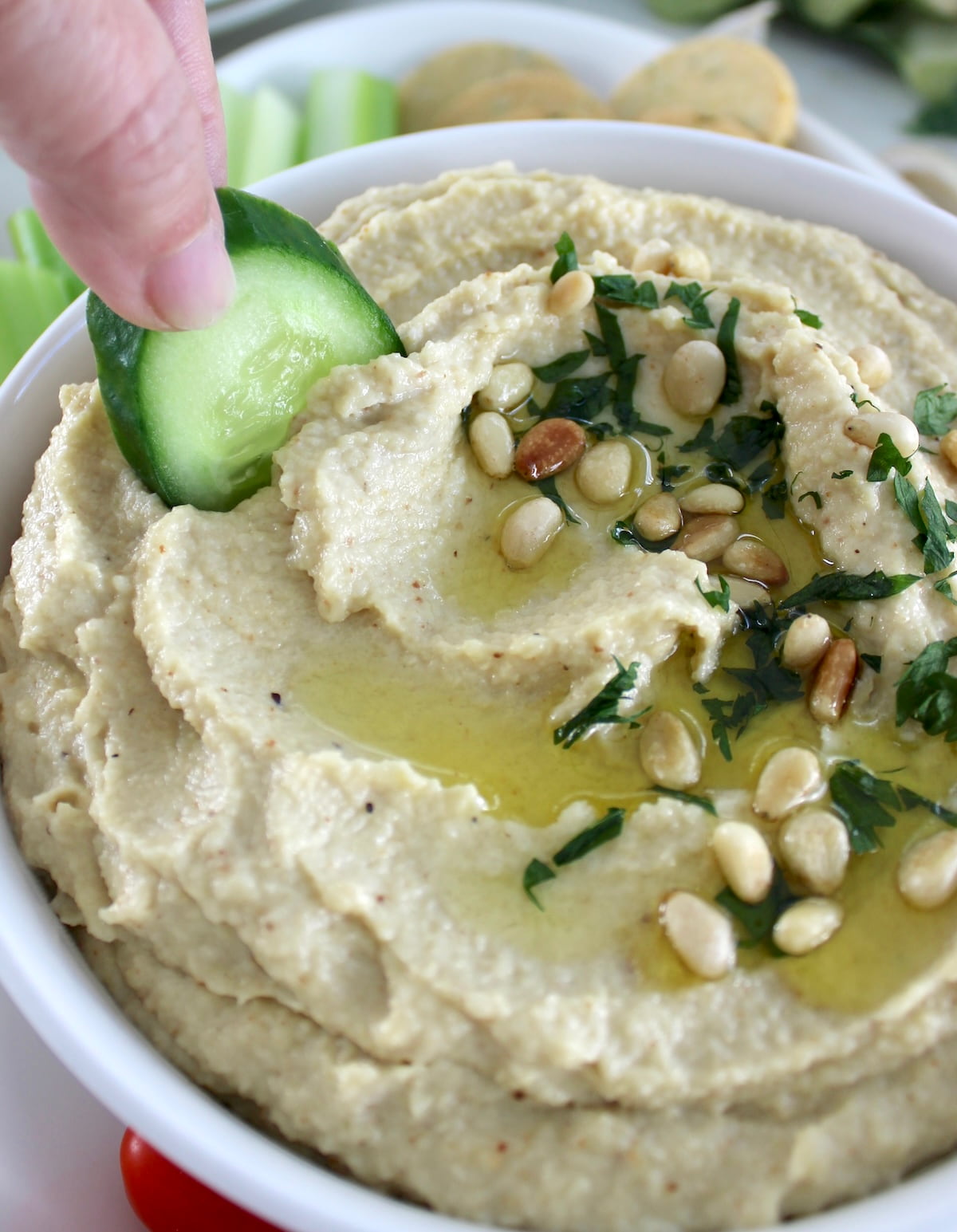 dipping cucumber in Roasted Garlic Cauliflower Hummus in white bowl