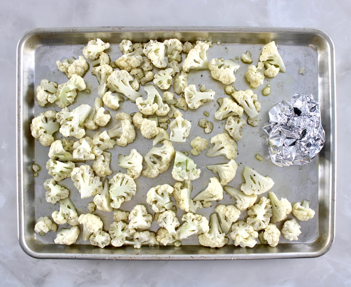 cauliflower florets on baking sheet with olive oil and ball on foil on the right