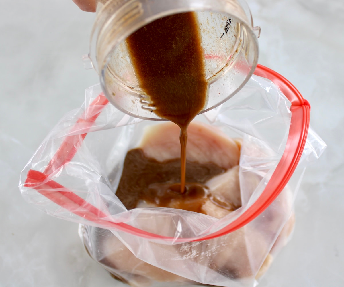 raw chicken in food storage bag with balsamic dressing pouring over the top