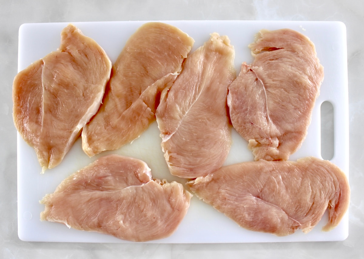 6 pieces of raw chicken breast on white cutting board