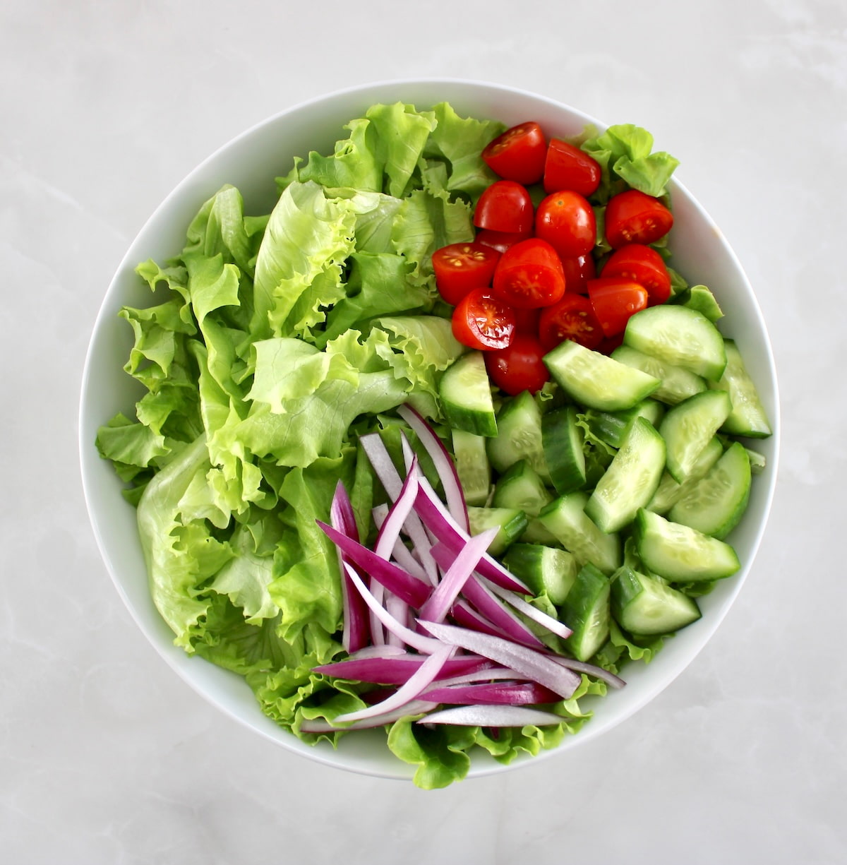 lettuce, chopped tomatoes, cucumbers and red onion in white bowl