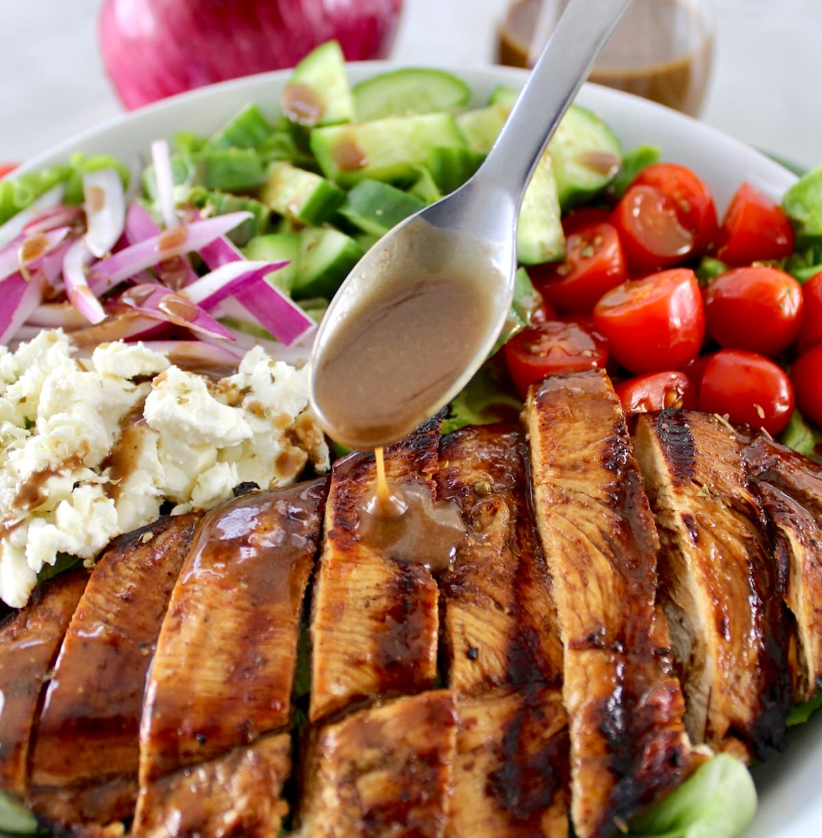 balsamic dressing being spooned over Balsamic Grilled Chicken Salad in white bowl