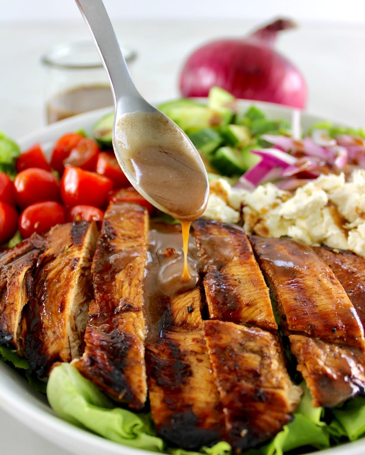balsamic dressing being spooned over Balsamic Grilled Chicken Salad in white bowl
