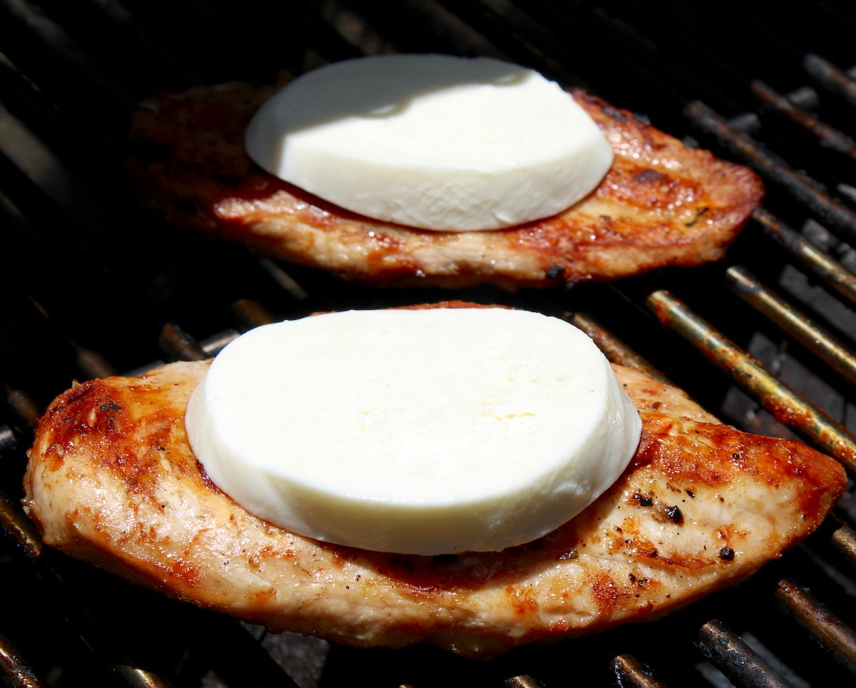 2 pieces of Grilled Chicken on grill with slice of fresh mozzarella on top
