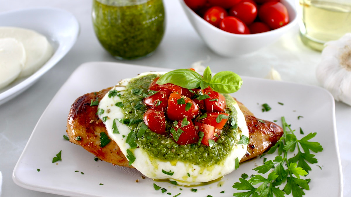 Grilled Chicken Margherita on white plate with pesto and tomatoes in back