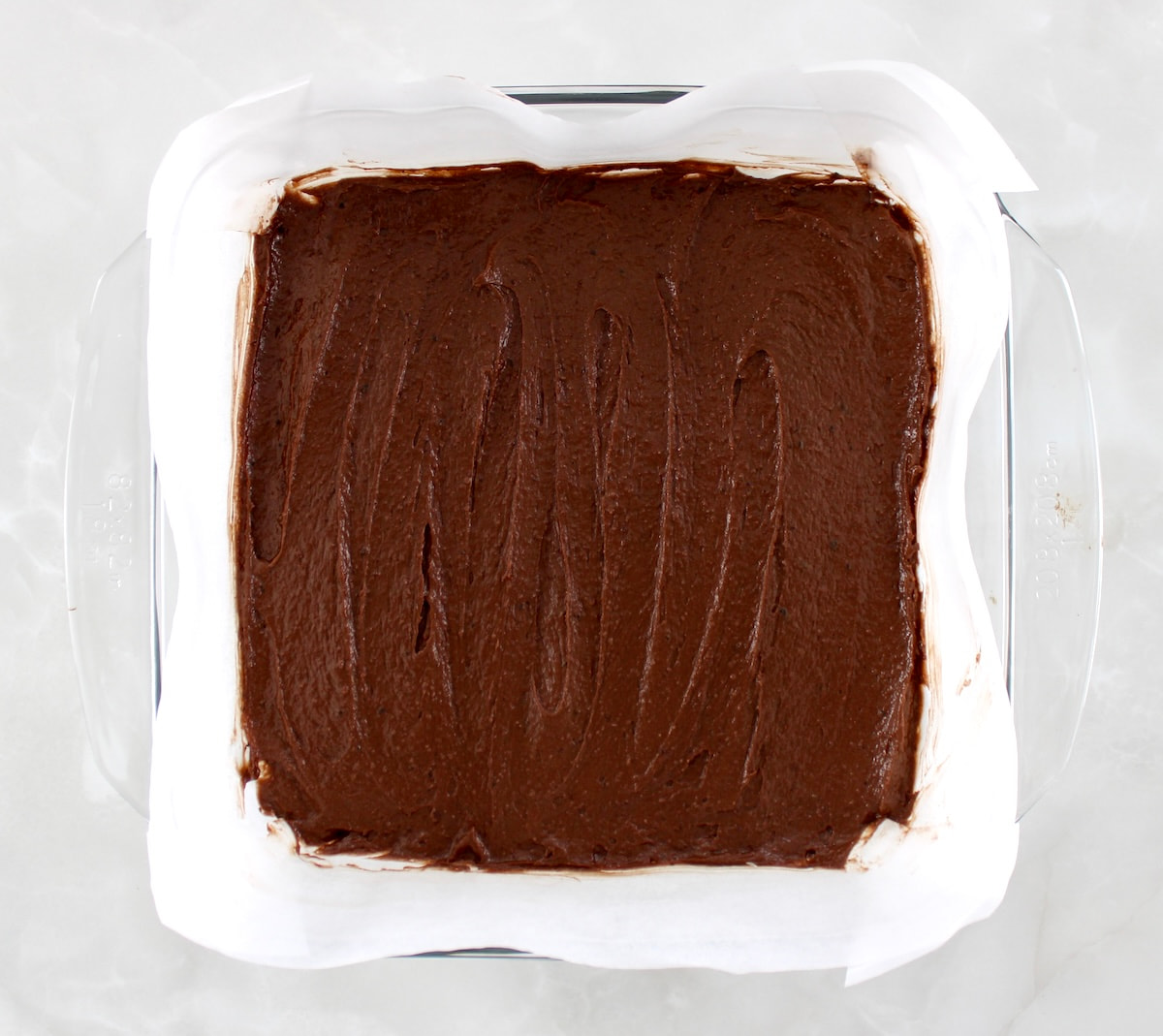 keto brownie batter in glass baking dish lined with parchment paper