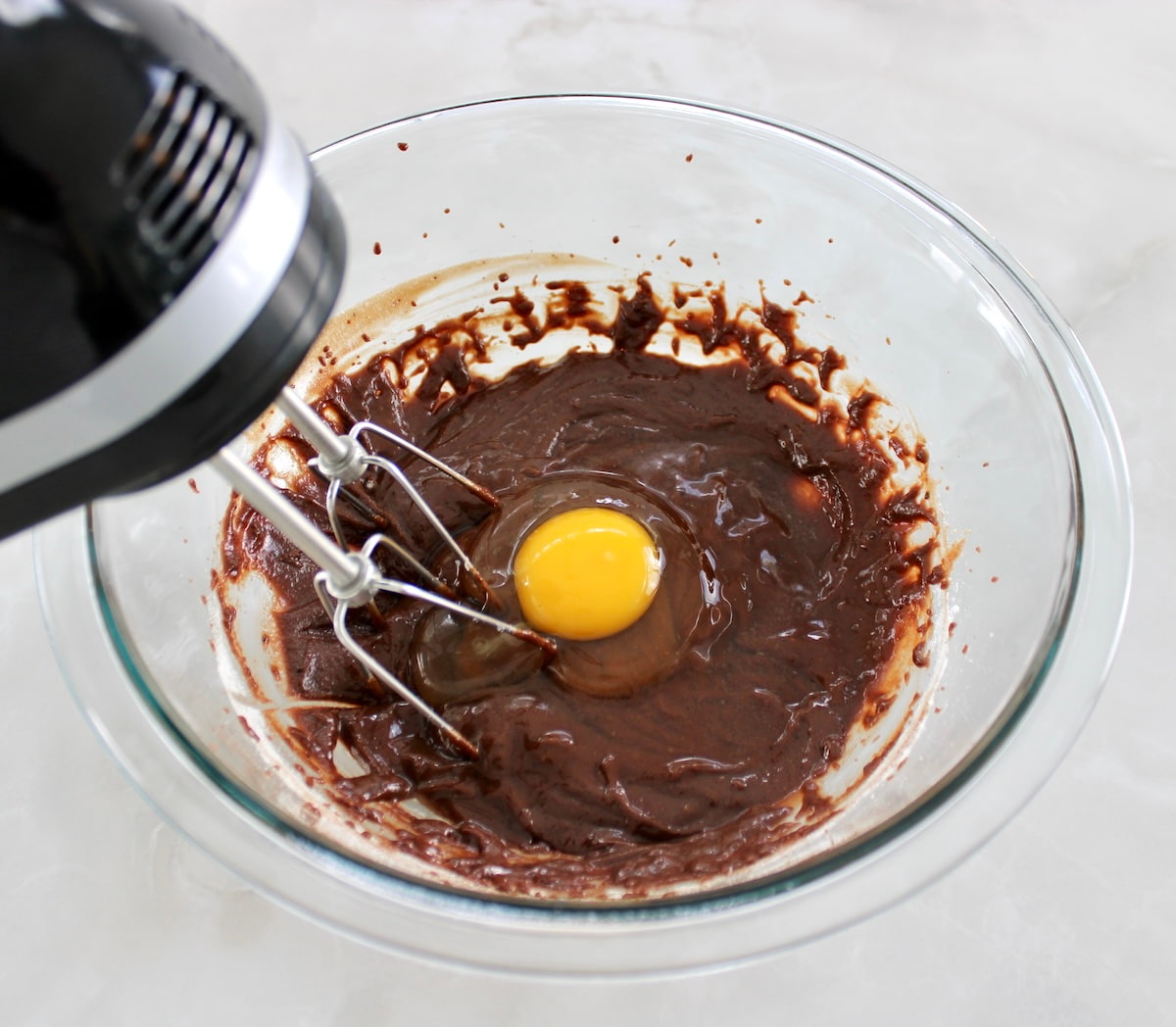 brownie batter with egg in glass bowl with hand mixer