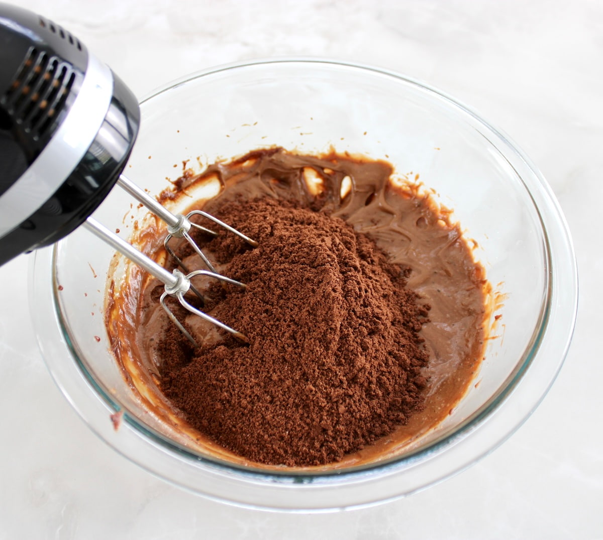 brownie batter with cocoa powder and almond flour in glass bowl with hand mixer