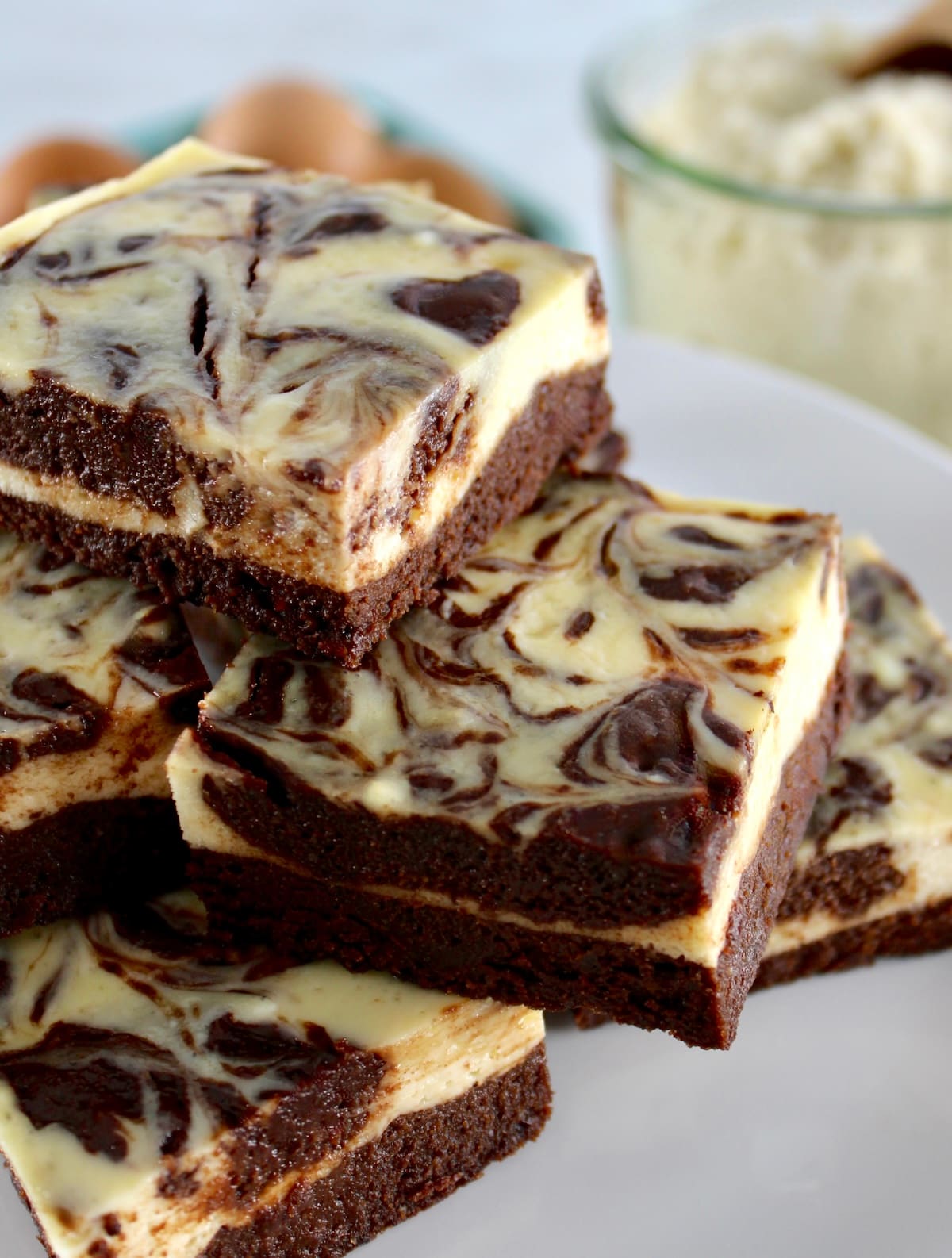closeup of Keto Cheesecake Brownie Bars stacked up on white plate with almond flour in back