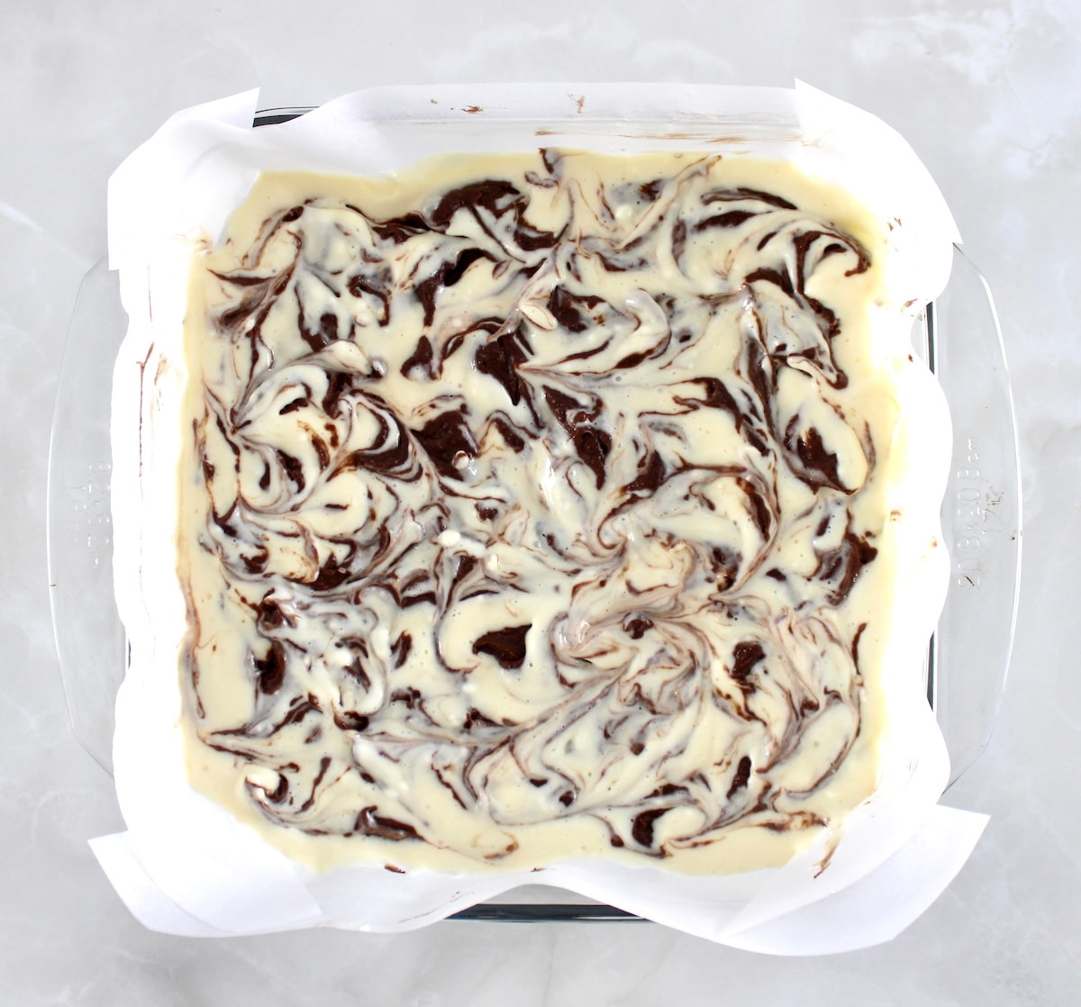 Keto Cheesecake Brownie Bars batter in parchment lined glass baking dish