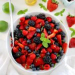 Keto Fruit Salad in white bowl with mint sprig on top and silver serving spoon on side