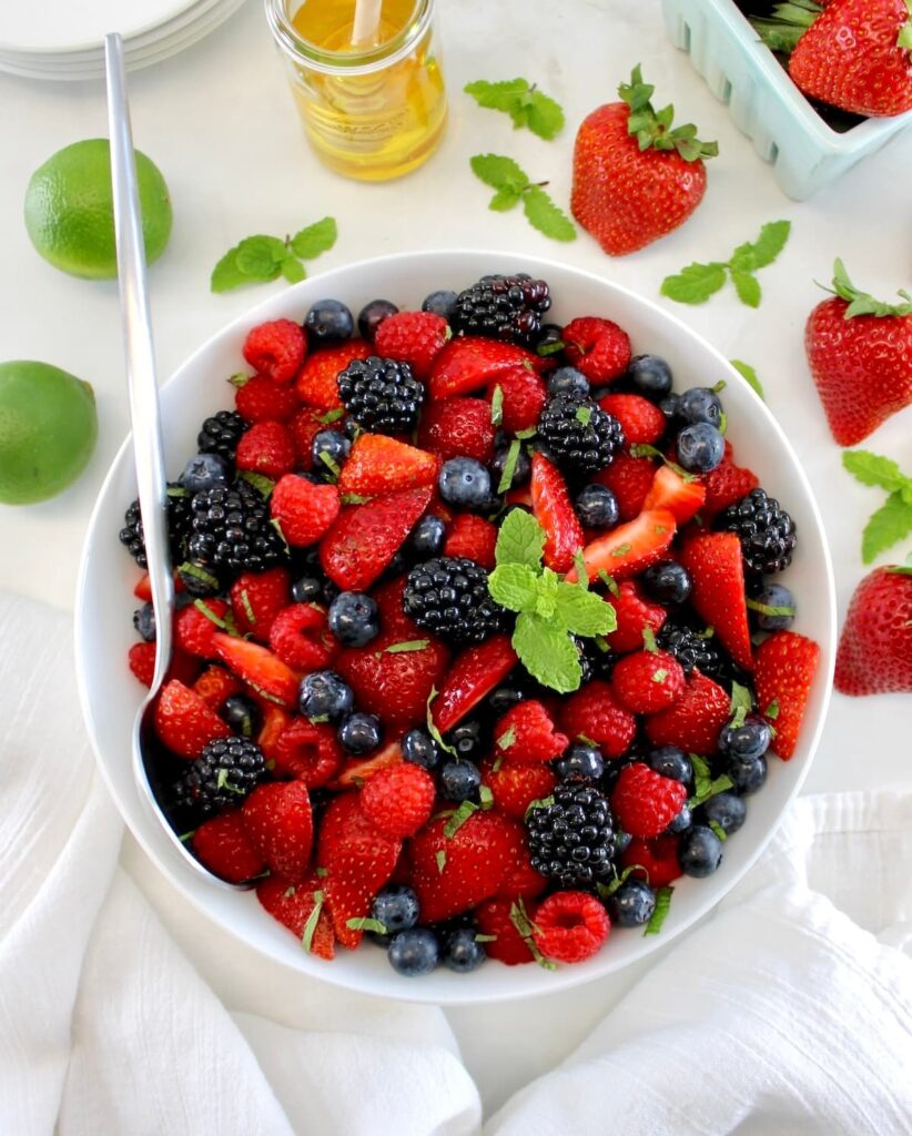 Keto Fruit Salad in white bowl with mint sprig on top and silver serving spoon on side