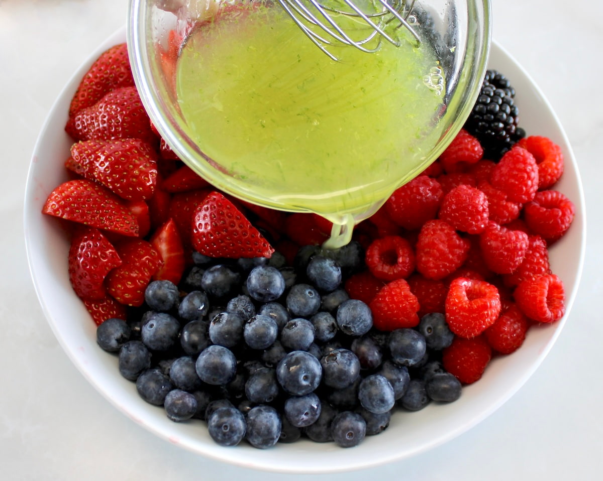 honey lime dressing being poured over Keto Fruit Salad in white bowl