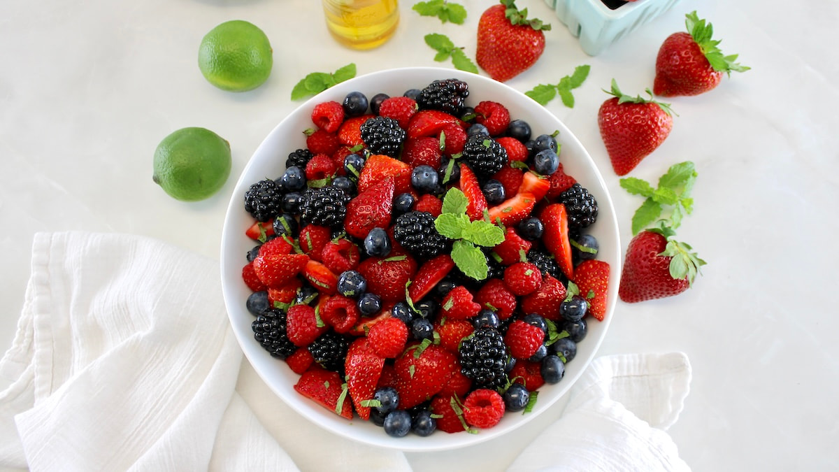 overhead view of Keto Fruit Salad in white bowl with strawberries and lime in back