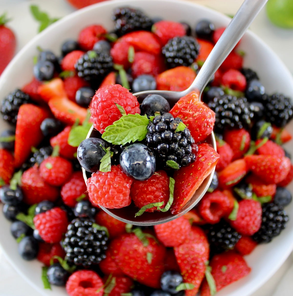 Keto Fruit Salad in spoon held up over white bowl