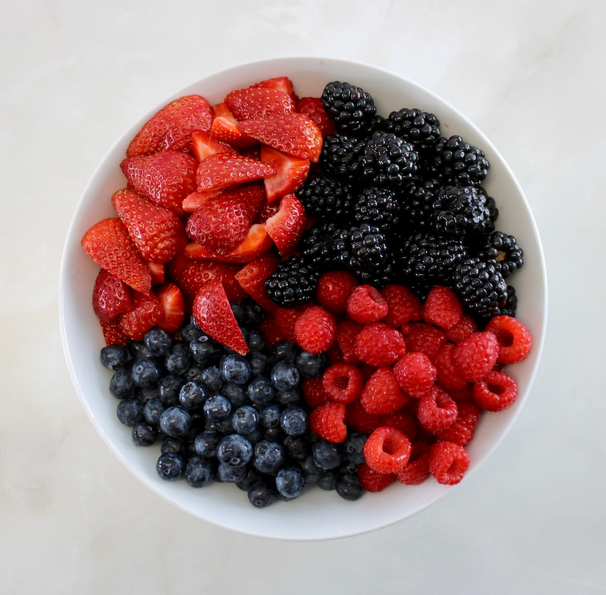 strawberries, blackberries, raspberries and blueberries in white bowl in groups