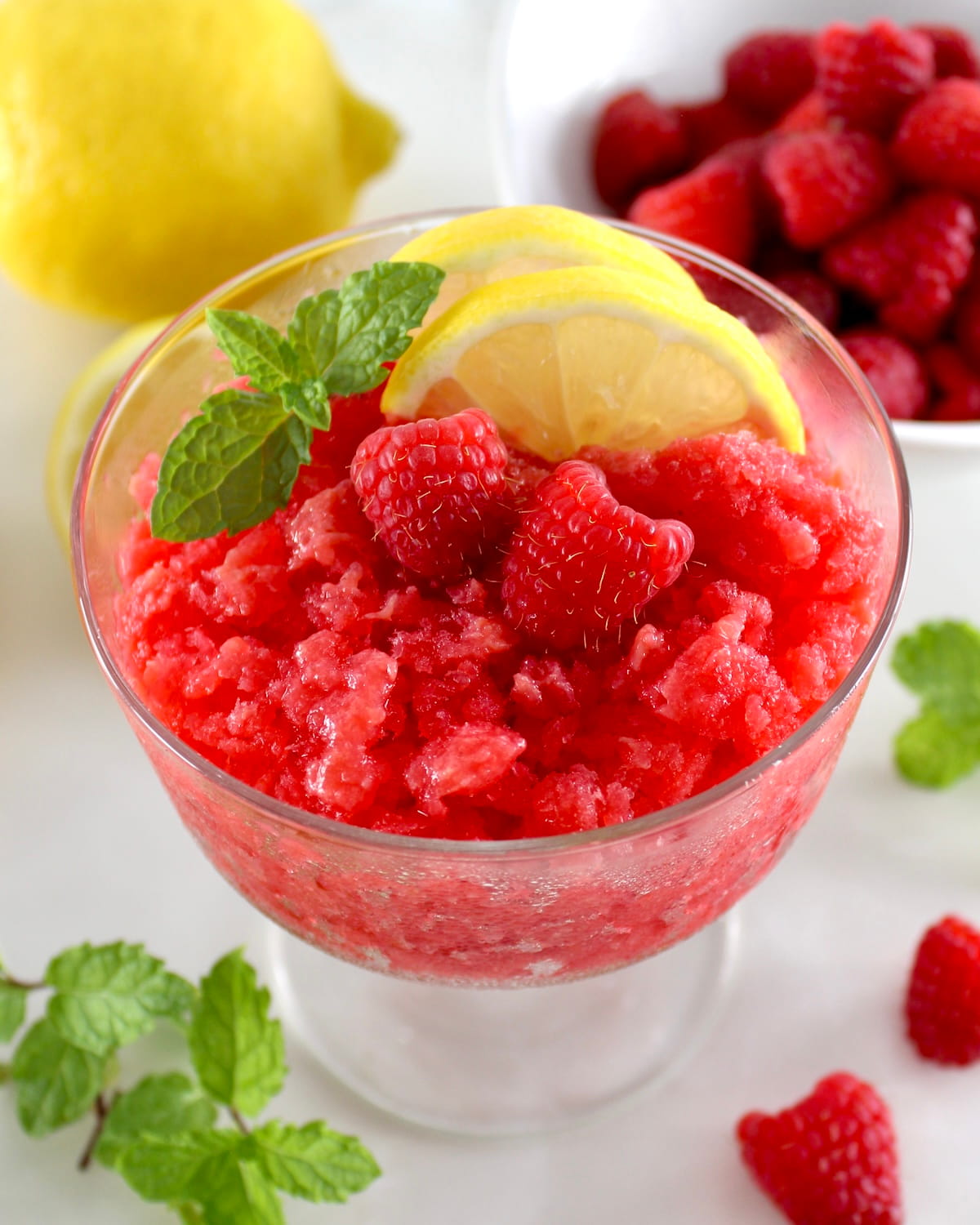 Raspberry Lemon Granita in glass with lemon slices, 2 raspberries and fresh mint on top