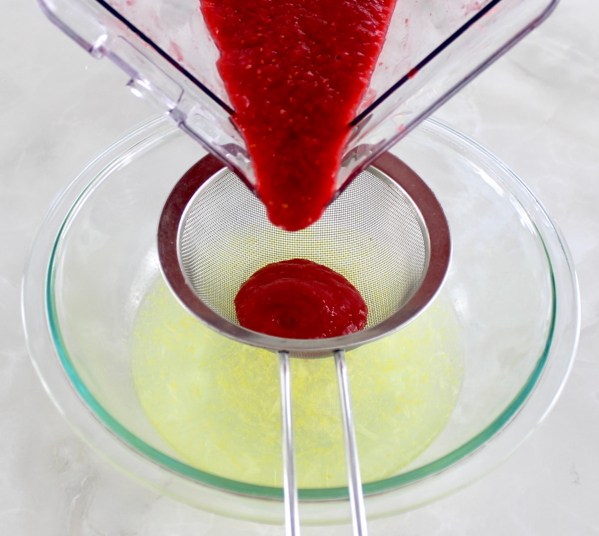 raspberry puree pouring into glass bowl with lemon water