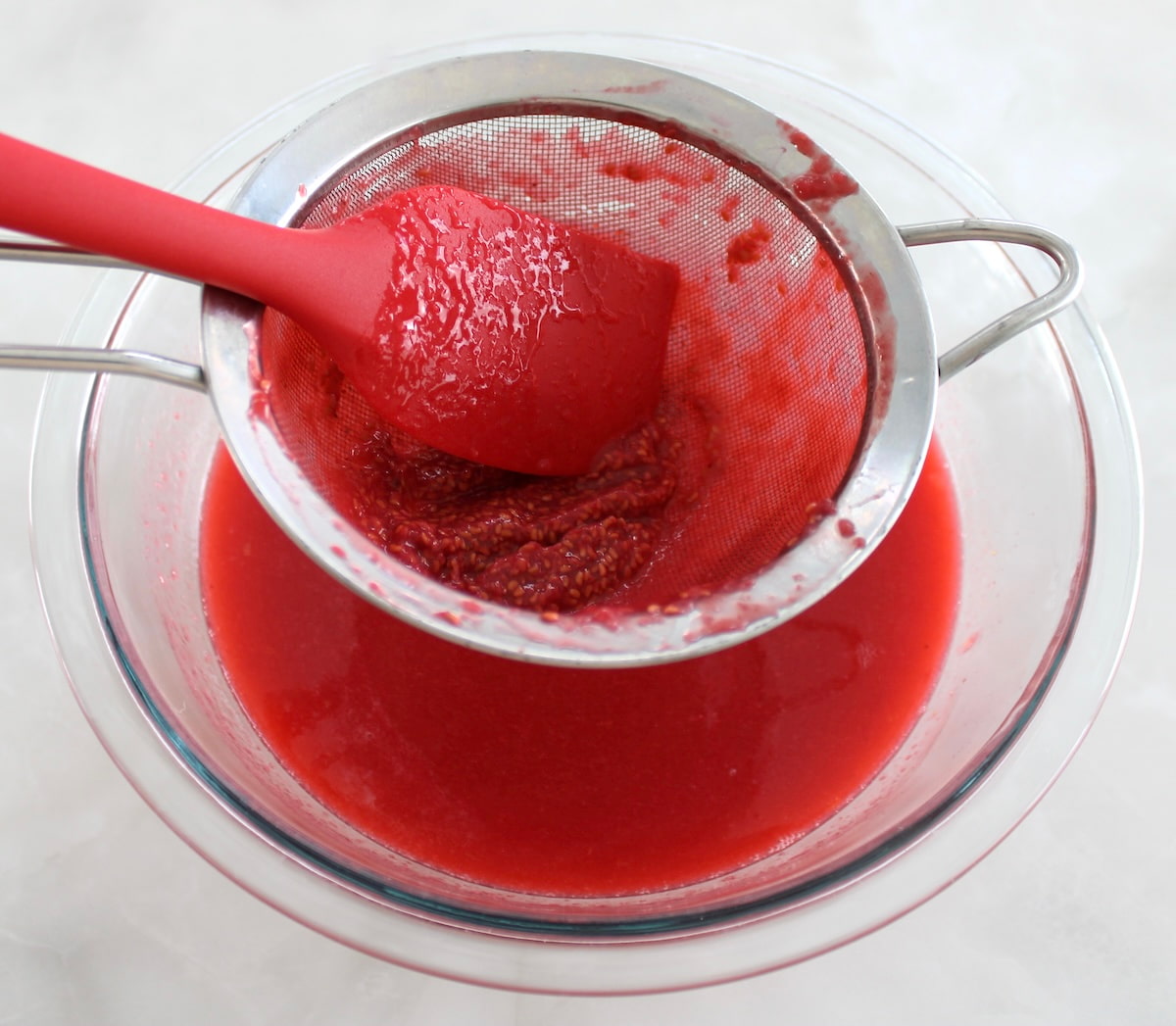 straining raspberry seeds in sieve over glass bowl
