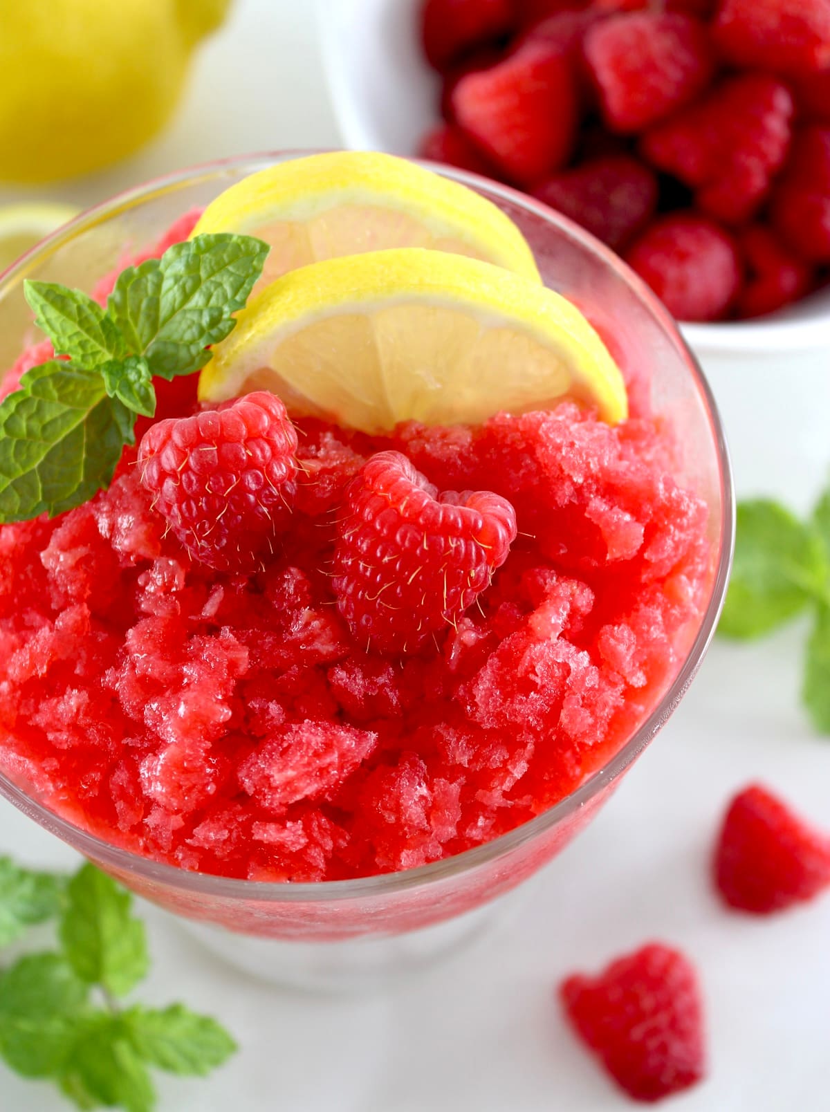 closeup of Raspberry Lemon Granita in glass with lemon slides and raspberries