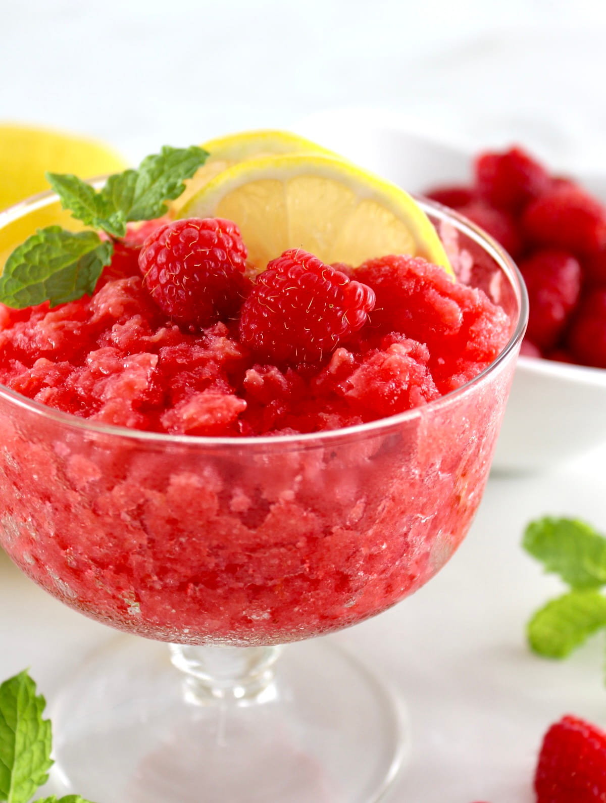 closeup side view of Raspberry Lemon Granita in glass with lemon, mint and raspberries on top