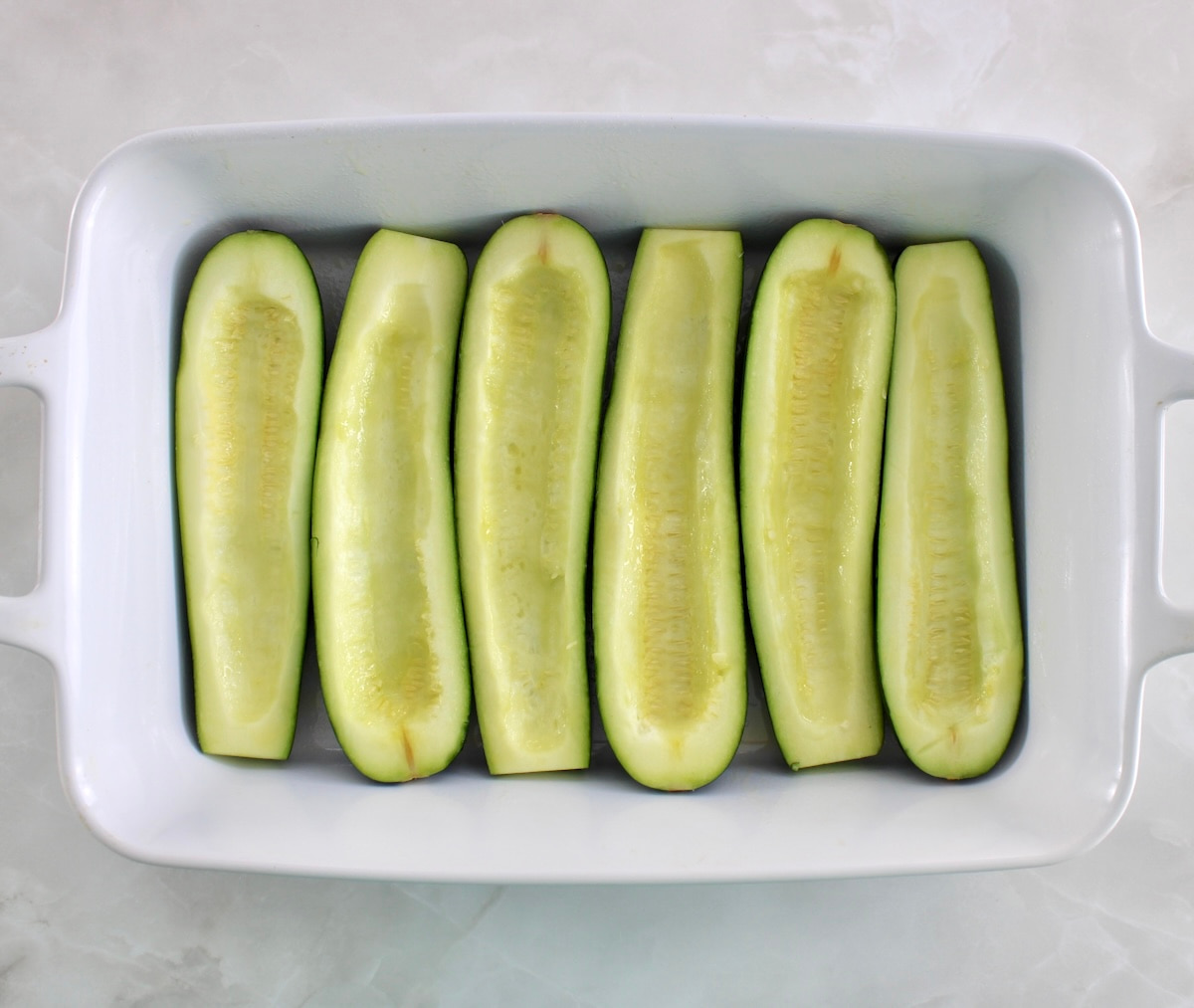 6 halves of zucchini in white casserole dish with centers scooped out