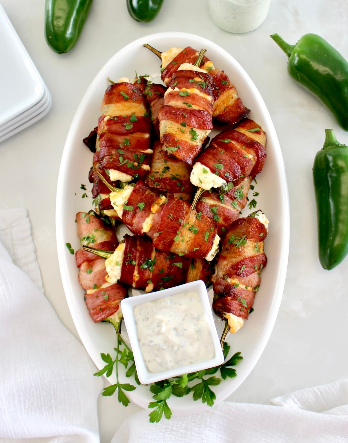 overhead view of Air Fryer Bacon Wrapped Jalapeño Poppers on white oval platter with ranch on side