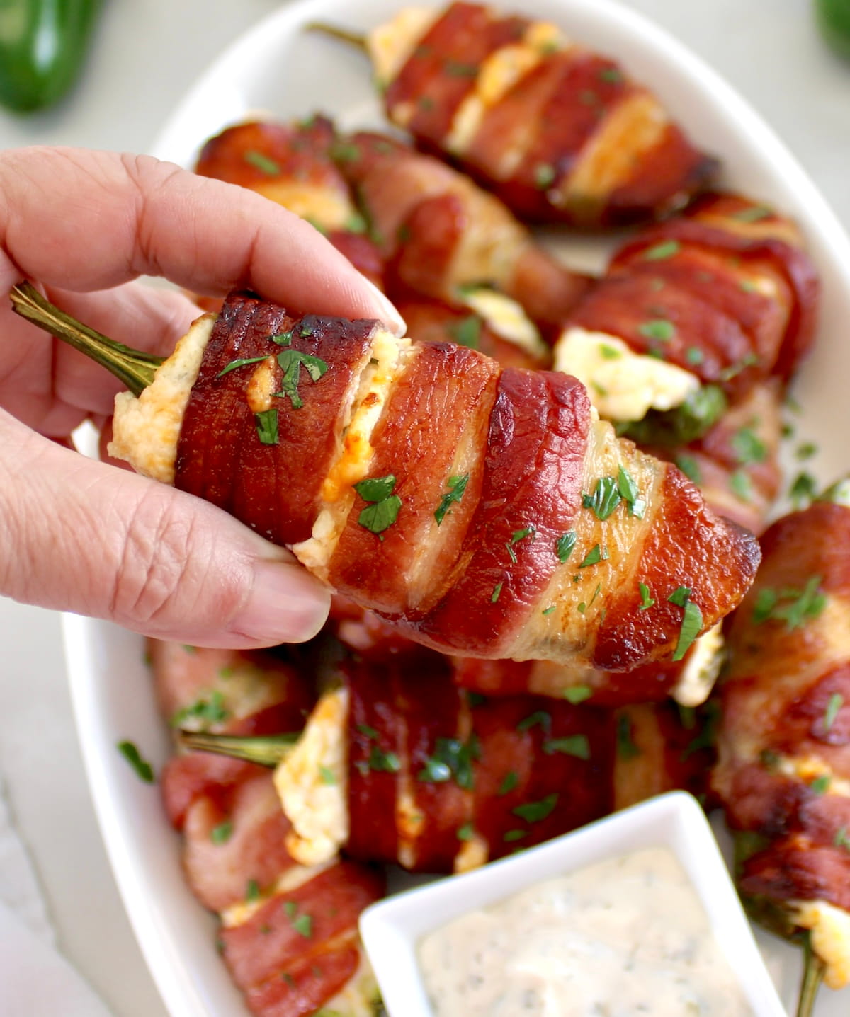 holding up Air Fryer Bacon Wrapped Jalapeño Popper with plate in background