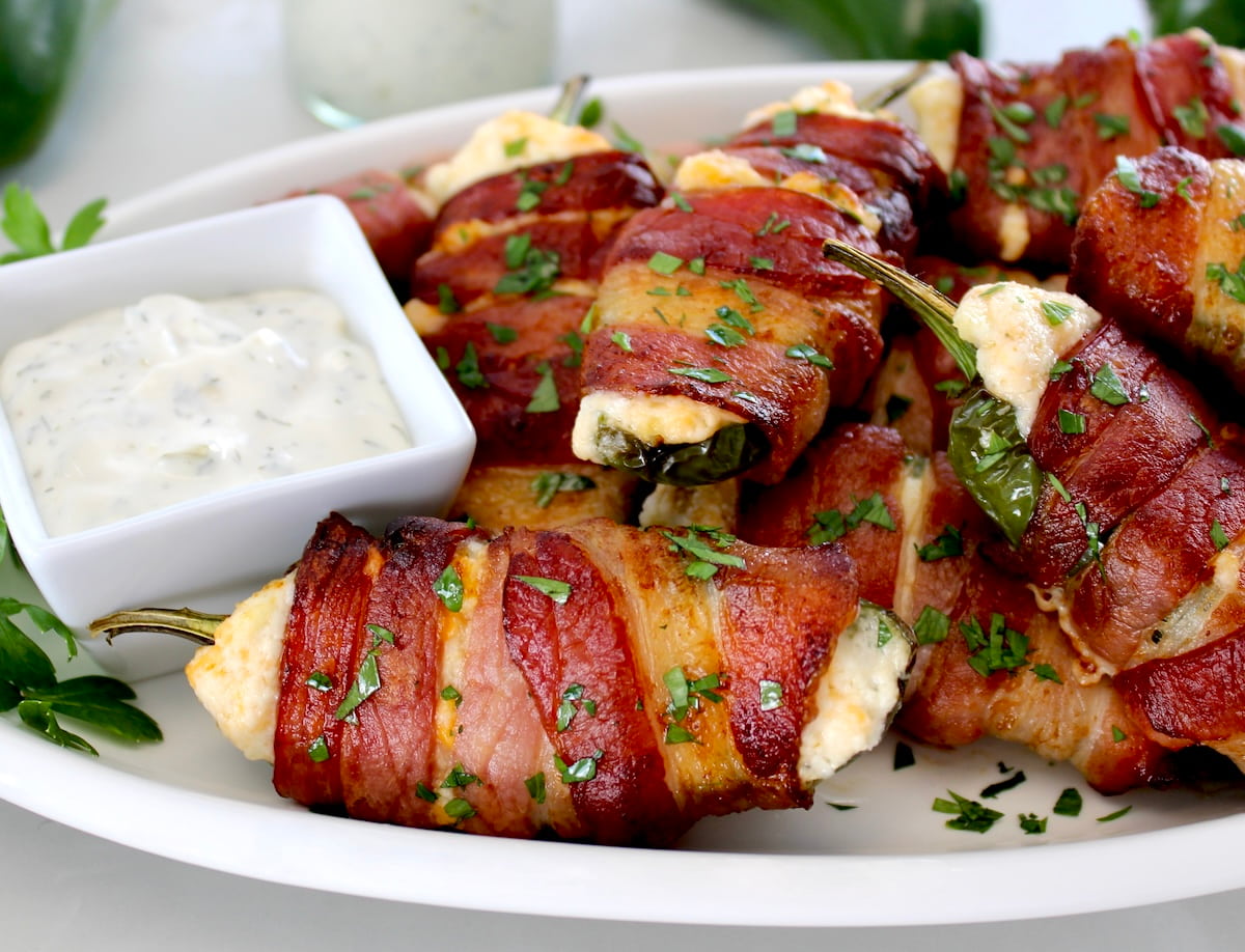 closeup of Air Fryer Bacon Wrapped Jalapeño Poppers on white plate with chopped parsley and ranch on side