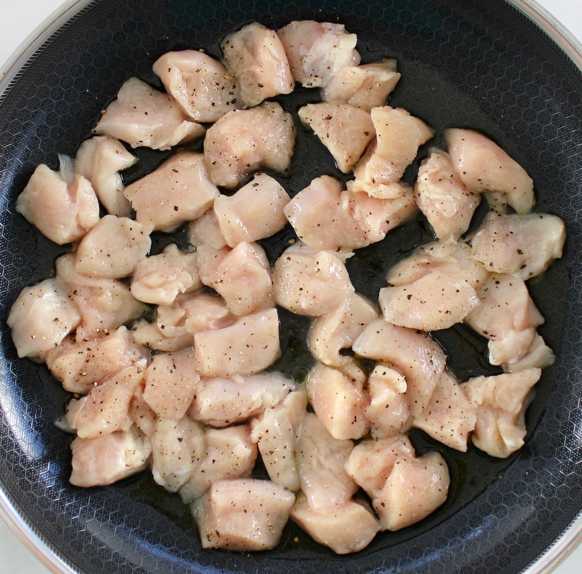 cut up raw chicken breast with salt and pepper in skillet