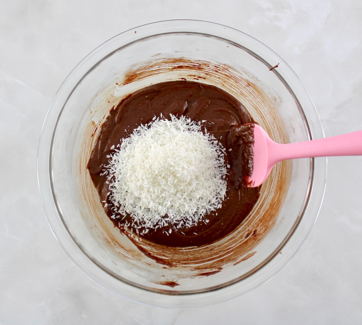 brownie batter and shredded coconut in glass bowl unmixed with pink spoon on side