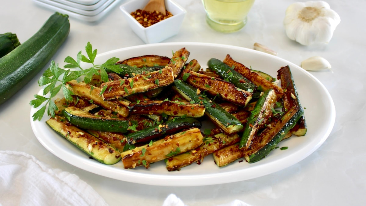 Easy Sautéed Zucchini in white oval platter with parsley garnish