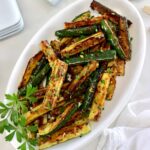 overhead view of Easy Sautéed Zucchini on white oval plate with parsley garnish