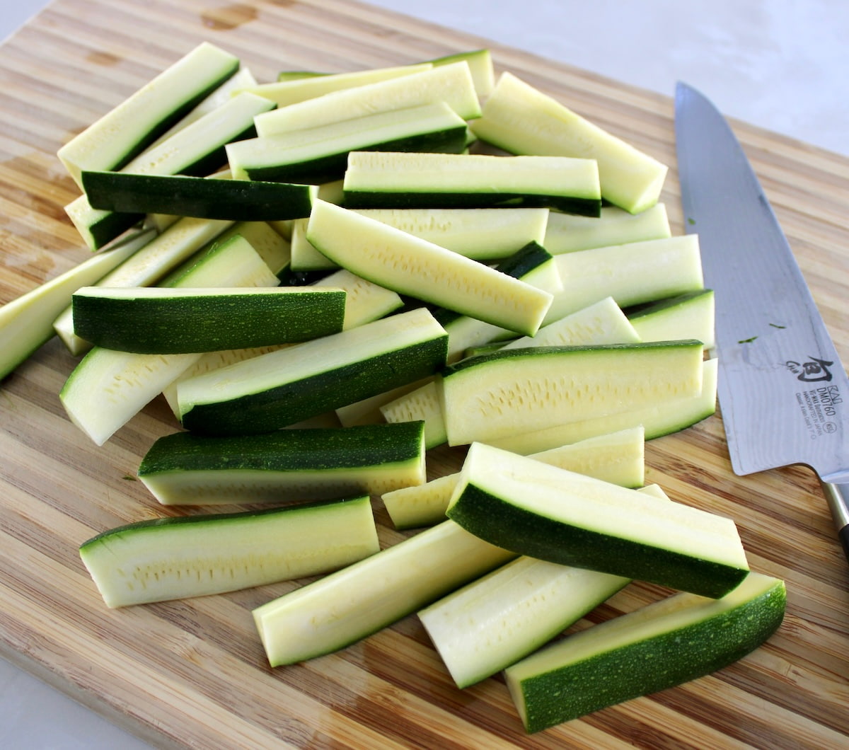 chopped zucchini sticks on cutting board with knife