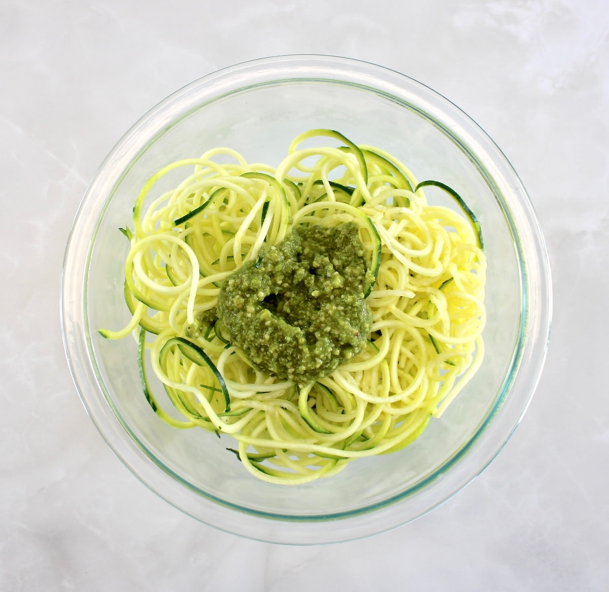 zucchini noodles in glass bowl with pesto on top